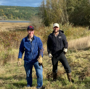 Image of two men near wetlands holding tree saplings.