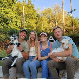 Four people and two goats posing for a photo